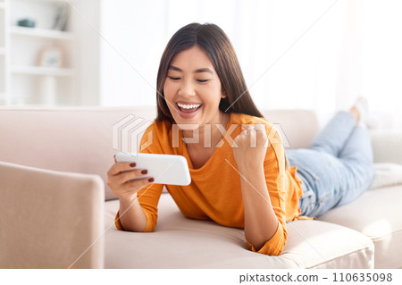 Emotional young asian woman gaming online, using smartphone 110635098