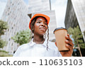 Happy black woman in helmet standing with coffee cup in daylight near buildings 110635103