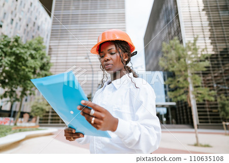 Professional female engineer in hardhat reading documents 110635108