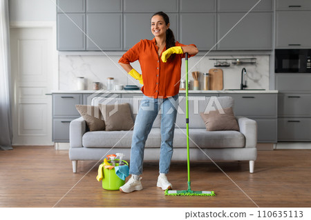 Confident woman with mop and cleaning gear in stylish kitchen Confident woman with mop and cleaning gear in stylish kitchen 110635113