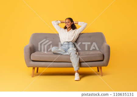 Relaxed black teenager girl resting sitting on couch, yellow backdrop Relaxed black teenager girl resting sitting on couch, yellow backdrop 110635131