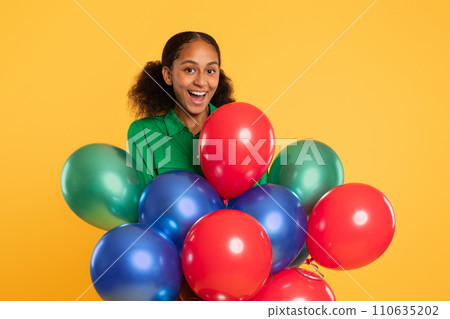 African teenager girl holds bunch of balloons over yellow background 110635202