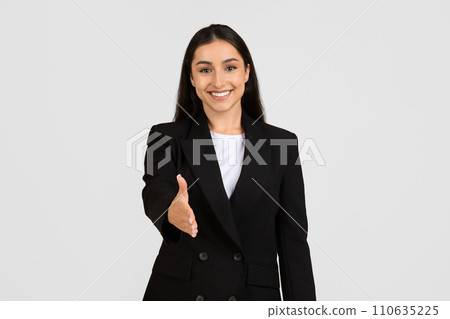 Happy young european businesswoman extending handshake with welcoming smile, posing on grey studio background 110635225