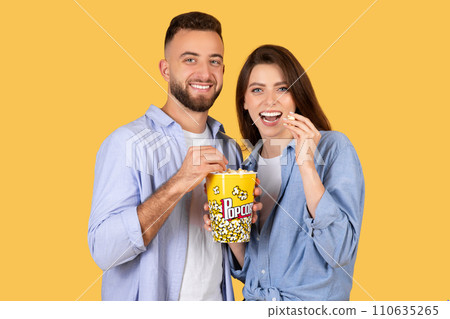 Couple sharing popcorn and smiles, enjoying movie night together 110635265