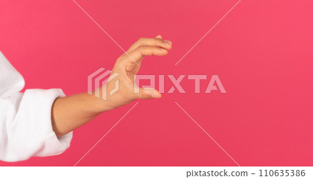 Female hand holding invisible object over pink background Female hand holding invisible object over pink background 110635386
