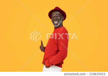 Cheerful senior man in a stylish red sweater and hat giving a thumbs-up sign 110635423