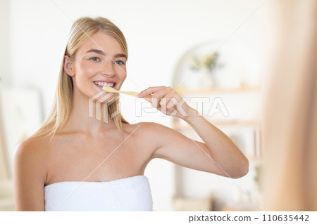 Young blonde lady maintaining oral health using tooth brush indoors 110635442