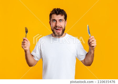 Hungry young guy holding knife and fork on yellow background 110635476