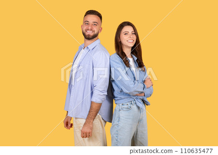 Happy couple standing back-to-back with confident smiles on yellow background 110635477