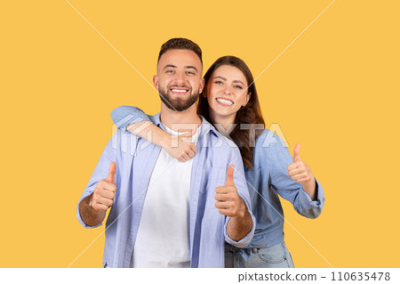 Enthusiastic couple giving thumbs up together on yellow background 110635478