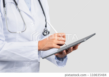 A professional female healthcare provider in a white lab coat uses a digital tablet with a stylus A professional female healthcare provider in a white lab coat uses a digital tablet with a stylus 110635484