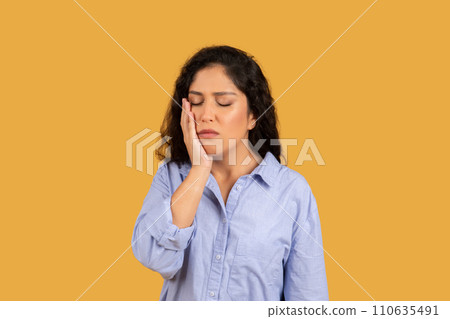 Woman with a pained expression, hand on her cheek, eyes closed, possibly suffering from a toothache Woman with a pained expression, hand on her cheek, eyes closed, possibly suffering from a toothache 110635491