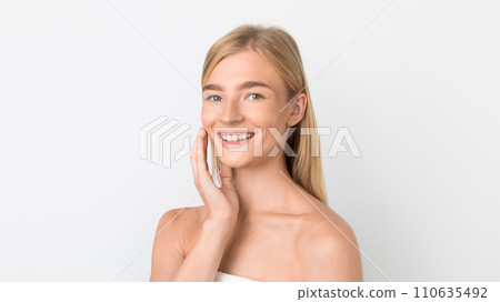 young woman applying moisturizer on face over white studio backdrop 110635492