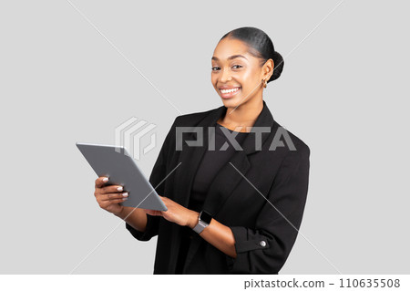 A confident young woman in business attire smiles while holding a tablet A confident young woman in business attire smiles while holding a tablet 110635508