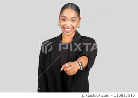 Engaging young woman in a tailored black blazer extends her arm confidently towards the camera 110635510
