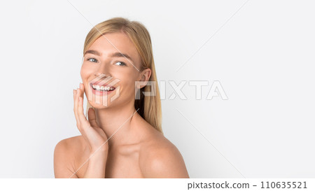 Young blonde woman smiling softly as she touches cheek, studio Young blonde woman smiling softly as she touches cheek, studio 110635521