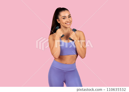 Smiling caucasian lady in sportswear doing exercises with hand dumbbells, enjoying workout on pink background 110635532