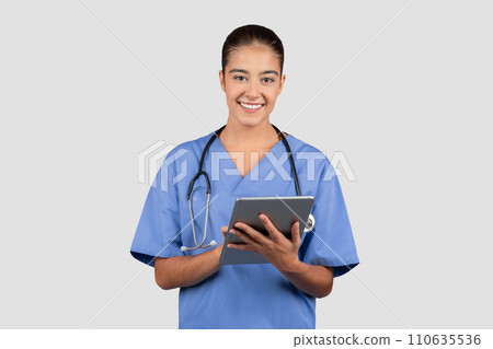Smiling, young, tech-savvy nurse in blue scrubs using a digital tablet, symbolizing modern healthcare 110635536