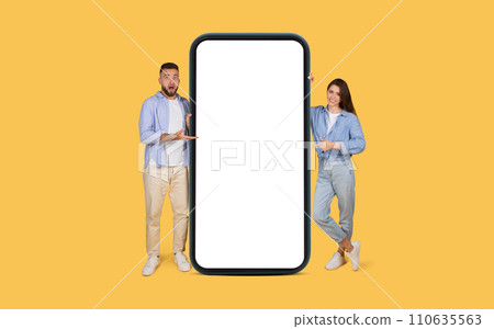 Shocked man and pointing woman with giant smartphone on yellow background Shocked man and pointing woman with giant smartphone on yellow background 110635563