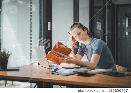 Portrait of a serious businesswoman using notebook and laptop computer in office..Portrait of a serious businesswoman using notebook and laptop computer in office.. 110636707