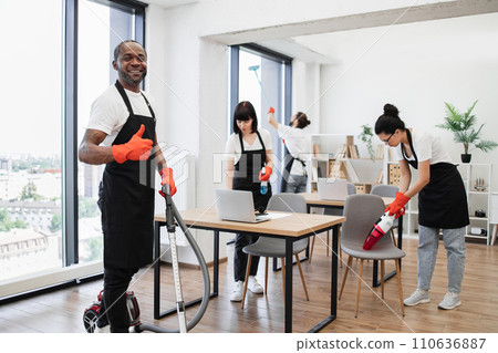 Side view of African American man using vacuum cleaner to clean floor from dirt. 110636887