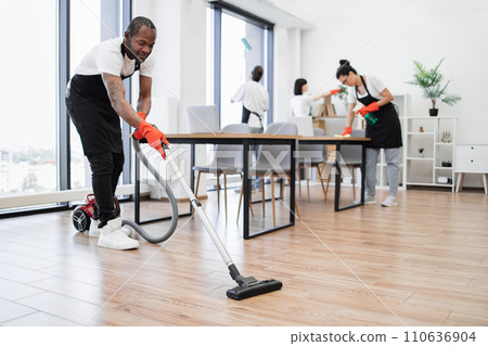 Side view of African American man using vacuum cleaner to clean floor from dirt. Side view of African American man using vacuum cleaner to clean floor from dirt. 110636904