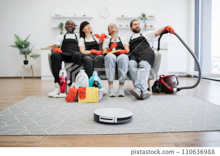 Focus on robot vacuum cleaner cleans floor while team of housekeepers resting. 110636988