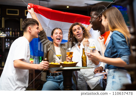 Young adults watching football championship in sports bar, supporting team from Netherlands 110637478