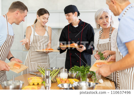 Smiling elderly woman talking to culinary enthusiasts during cooking masterclass 110637496