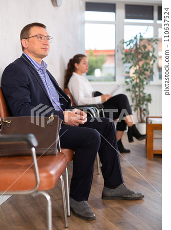 Middle-aged male visitor sitting on the bench in waiting room of clinic Middle-aged male visitor sitting on the bench in waiting room of clinic 110637524