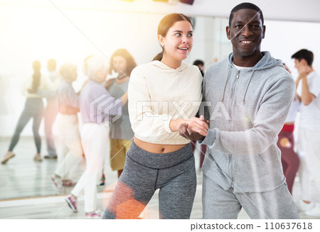 Happy african-american guy and caucasian girl practising paired latin dance in dance studio Happy african-american guy and caucasian girl practising paired latin dance in dance studio 110637618
