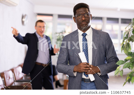 Upset middle-aged man standing in waiting room with his back to person who is shouting at him 110637745