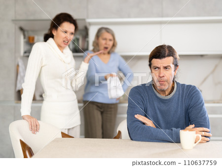 Wife and mother swear at man who puts up with it while sitting at kitchen table 110637759