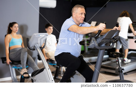 Man doing cardio workout out at gym, training on exercise bikes Man doing cardio workout out at gym, training on exercise bikes 110637780