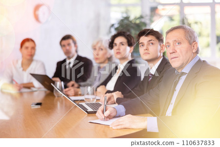 Elderly businessman listening to presentation of partners during meeting Elderly businessman listening to presentation of partners during meeting 110637833