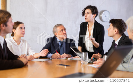 Focused colleagues of different ages discussing ideas and watching presentation while Latin female turning on presentation in meeting room Focused colleagues of different ages discussing ideas and watching presentation while Latin female turning on presentation in meeting room 110637841