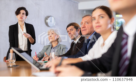Concentrated young adult old office workers sitting around the table and looking at screen while Latin female using projector remote control in office 110637946