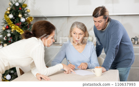 Married couple helps elderly mother write testament in kitchen at christmas Married couple helps elderly mother write testament in kitchen at christmas 110637993