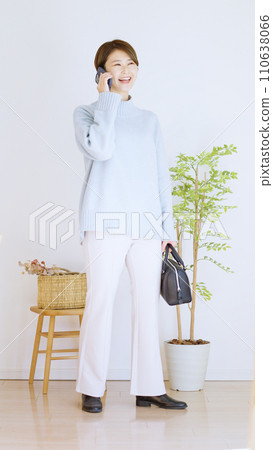 Full body of a woman in winter clothes using a smartphone (vertical orientation) 110638066