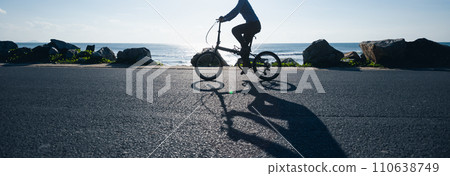 Riding folding bike on sunrise seaside road 110638749