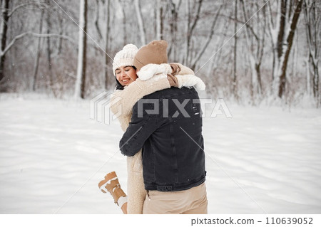 Young man and woman hugging and kissing outdoors. Romantic couple at winter in warm jackets walk in the park and hugging. Man and woman wearing winter clothes and knitted hats. 110639052