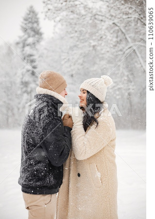 Young man and woman hugging and kissing outdoors. Romantic couple at winter in warm jackets walk in the park and hugging. Man and woman wearing winter clothes and knitted hats. Young man and woman hugging and kissing outdoors. Romantic couple at winter in warm jackets walk in the park and hugging. Man and woman wearing winter clothes and knitted hats. 110639065
