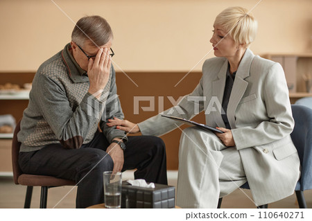 Portrait of mature man crying in therapy session with caring female psychologist supporting him, copy space 110640271