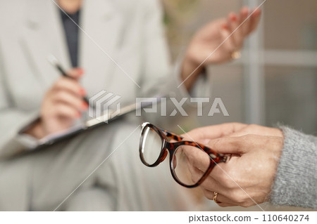 Detail shot of unrecognizable senior woman holding glasses in hand during consultation with doctor or therapist, copy space 110640274