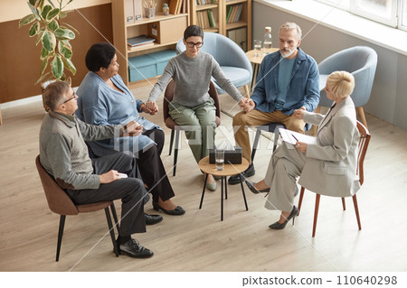 High angle view at group of senior people holding hands in therapy session and practicing meditation High angle view at group of senior people holding hands in therapy session and practicing meditation 110640298