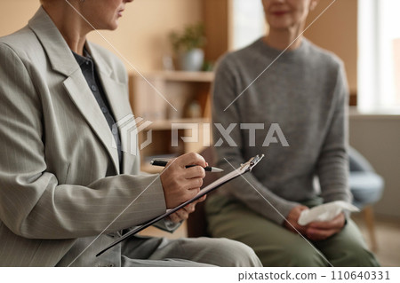 Side view closeup of female therapist holding clipboard and taking notes while leading support group meeting, copy space Side view closeup of female therapist holding clipboard and taking notes while leading support group meeting, copy space 110640331