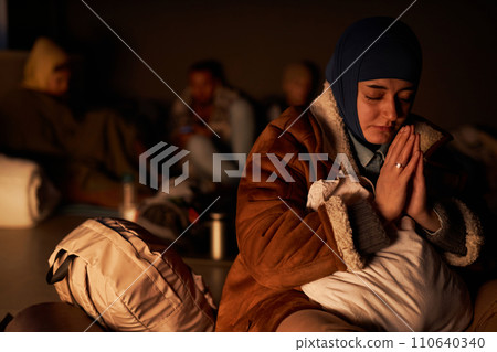Portrait of adult Middle Eastern woman praying in dark bomb shelter, copy space 110640340