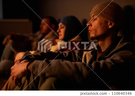 Diverse group of Middle Eastern people hiding in dark bomb shelter with young man in foreground 110640346