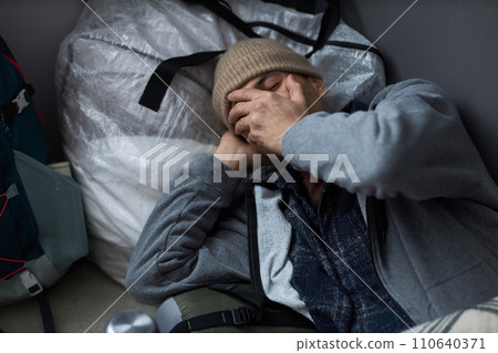 High angle portrait of distressed young man sleeping on floor at refugee shelter and covering face with hands 110640371