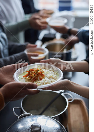 Vertical closeup of volunteers helping at soup kitchen and giving out hot meals, focus on hands holding plate with rice 110640425